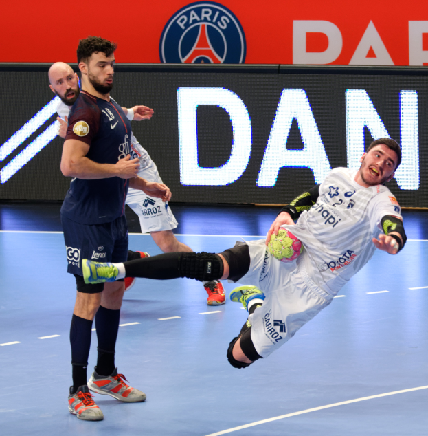 Eine Gruppe von Männern, die auf einem Handballfeld spielt, einer hält einen Ball, mit einem Hintergrundschild der Paris Saint-Germain Futsal-Mannschaft.