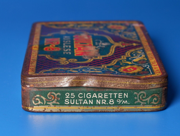 Ein kleiner Blechdosen mit Zigaretten auf einem blauen Tisch mit Text darauf.