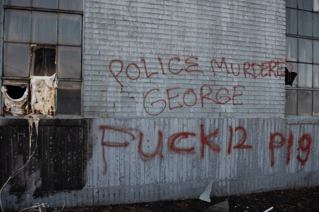 Graffiti auf einer Gebäudewand mit der Aufschrift "Polizeimord George Fuck 12 P19" mit Fenstern und verstreuten Gegenständen davor.