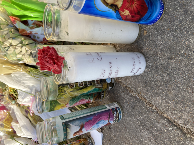 Makeshift roadside memorial with glass bottles featuring photos and text, a floral bouquet, and lit candles.