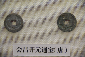 Zwei chinesische Münzen in einem Museum ausgestellt, auf einem Tuch mit einer Texttafel im Hintergrund.