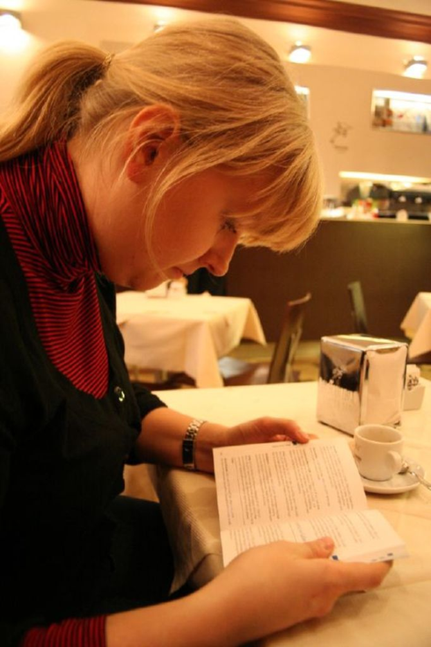 Eine Frau sitzt auf einem Stuhl und hält ein Buch auf einem Tisch, auf dem auch eine Tasse und ein Fußball stehen.