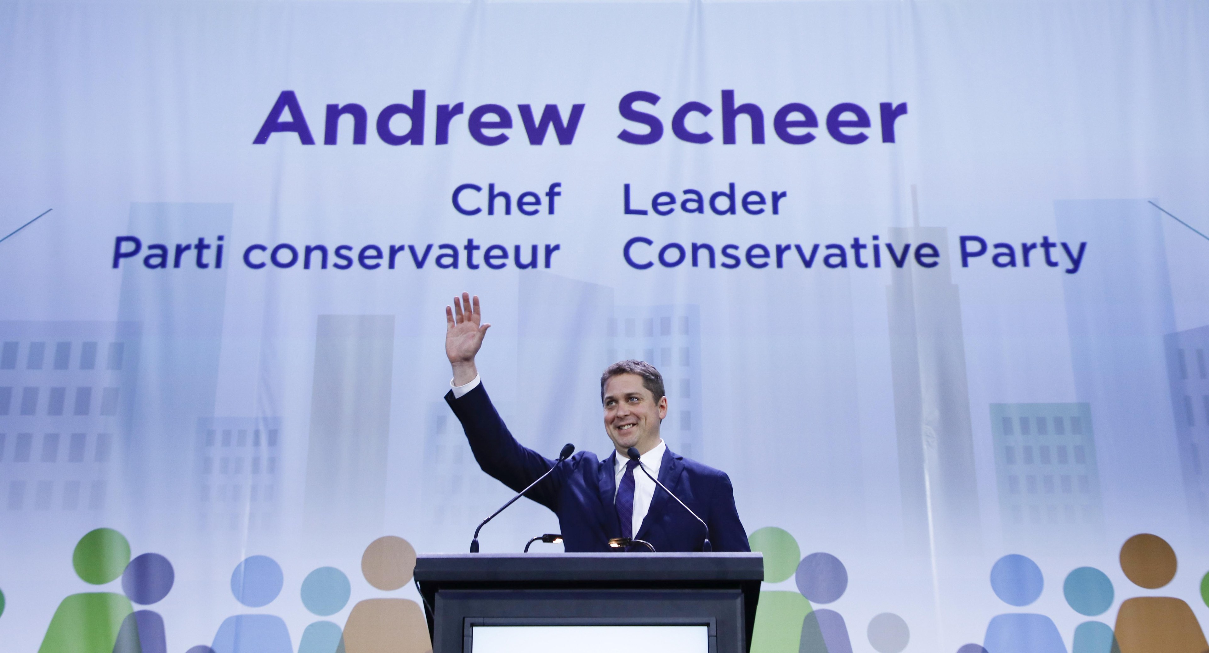 Konservative-Parteichef Andrew Scheer steht an einem Podium mit zwei Mikrofonen und einem Bildschirm dahinter, mit einem Banner mit Text und Gebäudeillustrationen im Hintergrund.