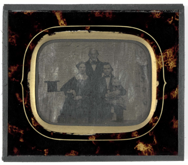 Schwarz-weißes Foto eines Mannes in Anzug und Krawatte und einer Frau in unbekannter Kleidung, die vor einem Fernseher stehen und ernste Gesichter haben.