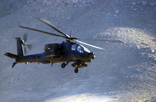 Ein schwarzer Hubschrauber mit rotierenden Rotorblättern fliegt über ein Gebirgsmassiv mit felsigem Hintergrund.