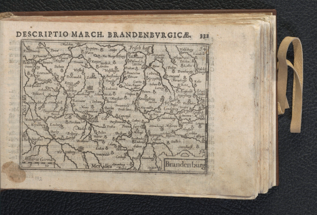 Ein offenes Buch, das eine detaillierte Karte der geografischen Merkmale von Brandenburg zeigt, liegt auf einer schwarzen Oberfläche.