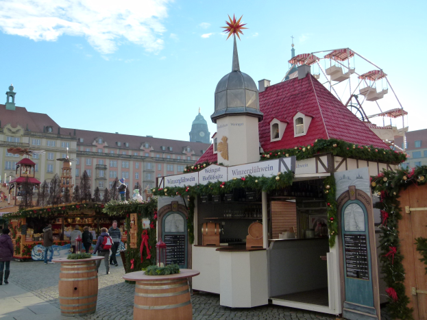 Ein geschäftiger Weihnachtsmarkt in Nürnberg, Deutschland mit Menschen um dekorierte Stände, festliche Lichter, Schmuck, Gebäude mit Fenstern, ein großes Rad und einen bewölkten Himmel, mit einer Tafel mit Text auf der rechten Seite.