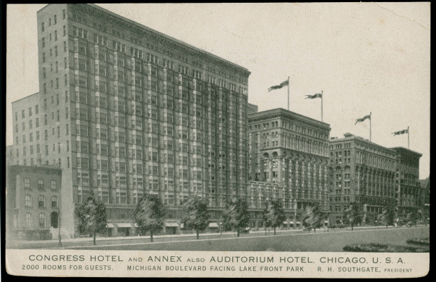 Schwarzes und weißes Foto des Congress Hotels und des Annex Auditorium Hotels in Chicago, ein großes Gebäude mit vielen Fenstern, umgeben von Bäumen und Fahnenmasten, mit einem klaren Himmel im Hintergrund und Text unten.