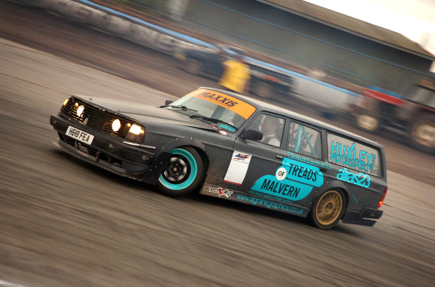 Ein Auto mit Fahrer fährt auf einer Rennstrecke, umgeben von anderen Fahrzeugen, mit einem unscharfen Hintergrund aufgrund der Bewegung.