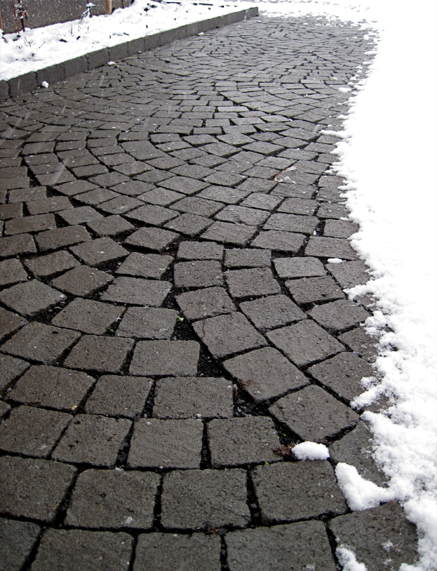 Eine Kopfsteinpflasterstraße mit leichtem Schnee auf dem Boden und einem Zaun im Hintergrund, der eine friedliche Winterszene schafft.