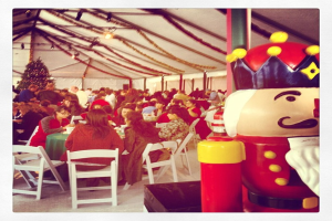 Eine Gruppe von Menschen feiert Weihnachten in einer Hütte, mit einem geschmückten Baum, weißen Stühlen, einem roten Spielzeug-Sicherheitswächter und einer schwarzen Krone.