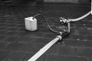 Ein Schwarz-Weiß-Foto eines Gasbehälters mit einem daran befestigten Schlauch vor einem Gebäude mit einer Tür.