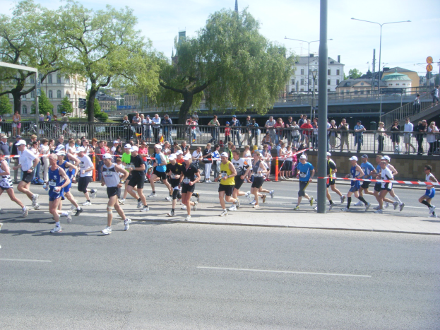 Gruppe von Läufern bei einem Marathon auf einer Straße mit Zuschauern, Absperrungen und einer Ziellinienbinde.