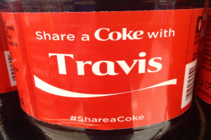 Eine Coca-Cola-Flasche mit der Aufschrift "Teile eine Coke mit TRAVIS" darauf gedruckt.