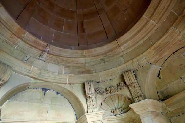 Innenansicht eines alten Gebäudes mit einem steinernen Bogengang, Kuppel und Wänden mit kunstvollen Verzierungen.