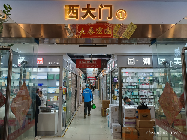 Innenansicht einer chinesischen Apotheke mit Glaswänden, einer Pflanze links, Regalen mit Artikeln, verstreuten Kartons und einem Namensschild oben.