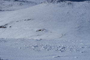 Ein schneebedeckter Berg mit einigen Skifahrern, die hinunterfahren, unberührter Schnee und ein strahlend blauer Himmel, mit schneebedeckten Bergen im Hintergrund.