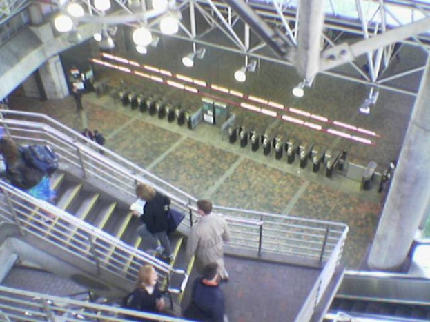 Ein Zugangstor in einem Flughafen mit Menschen auf einer Treppe unten und Lampen und Eisenstangen oben.