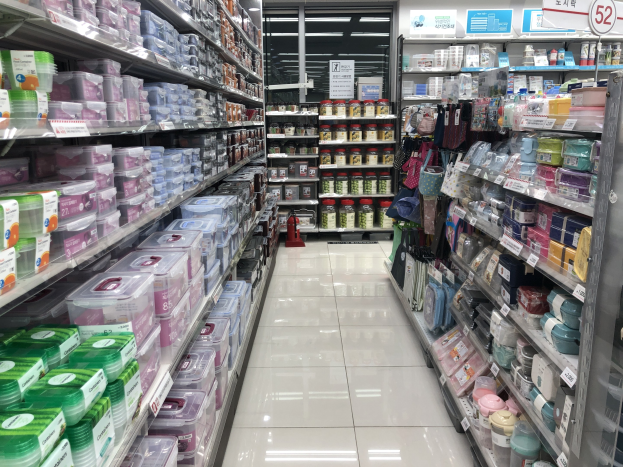 Ein chinesischer Supermarktgang mit Regalen voller Kisten, Flaschen, Tüten und anderen Artikeln, mit beleuchteten Schildern, Deckenleuchten und einem sichtbaren Feuerlöscher auf dem Boden.