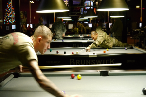 Ein Raum mit Snookertischen, Spieler auf beiden Seiten, hängende Lampen, ein Weihnachtsbaum in einer Ecke und Bildschirme mit Ergebnissen.