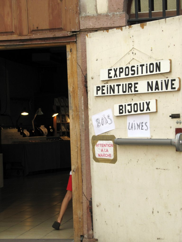 Ein Innenblick in ein Obdachlosenheim mit einer Person im Hintergrund neben Treppe und Lampen und einer Tür auf der rechten Seite mit Brettern und Text.