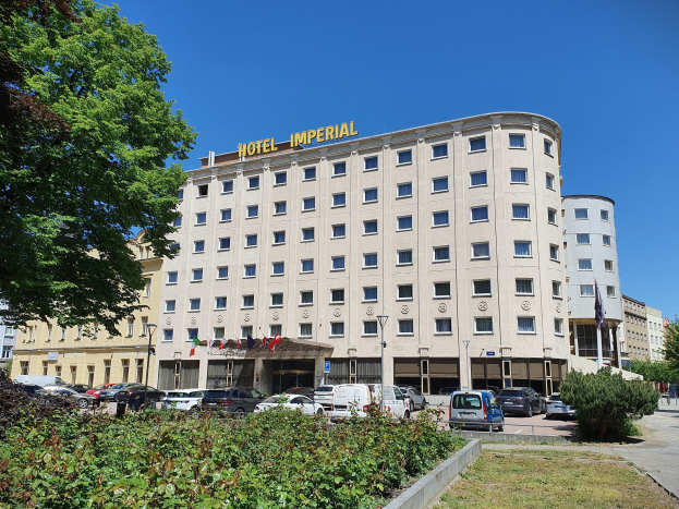 Das Kaiserhof-Hotel in Berlin, Deutschland, ein große Gebäude mit Fenstern, umgeben von Grün, geparkten Autos, Straßenmasten mit Flaggen, unter einem bewölktem Himmel.
