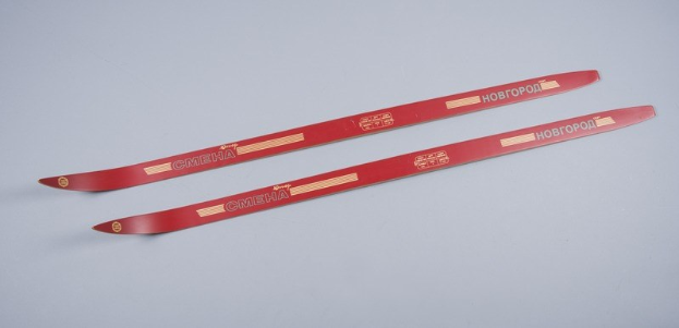 Zwei rote Ski mit Textmarkierungen übereinandergestapelt auf einer weißen Oberfläche.