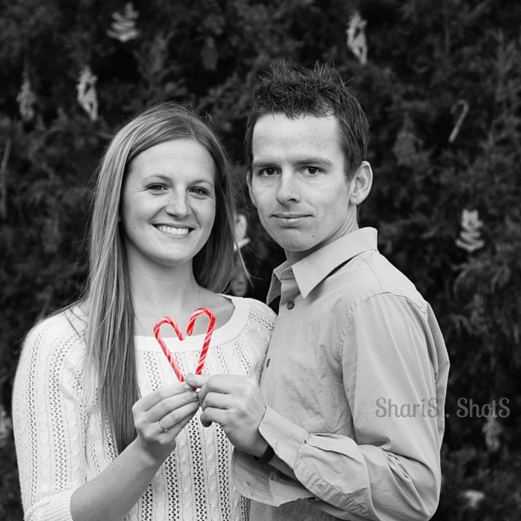 Ein Mann und eine Frau stehen draußen und halten je einen Strohhalm in der Hand, im Hintergrund ein Weihnachtsbaum.