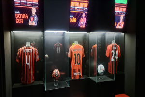 Eine Vitrine voller Fußballtrikots, die von Schaufensterpuppen getragen werden, mit einem Fußball in den Glasboxen und Bildschirmen oben, die Texte und Bilder von Spielern zeigen, wahrscheinlich repräsentierend Valencia CF.