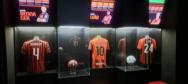 Eine Vitrine voller Fußballtrikots, die von Schaufensterpuppen getragen werden, mit einem Fußball in den Glasboxen und Bildschirmen oben, die Texte und Bilder von Spielern zeigen, wahrscheinlich repräsentierend Valencia CF.