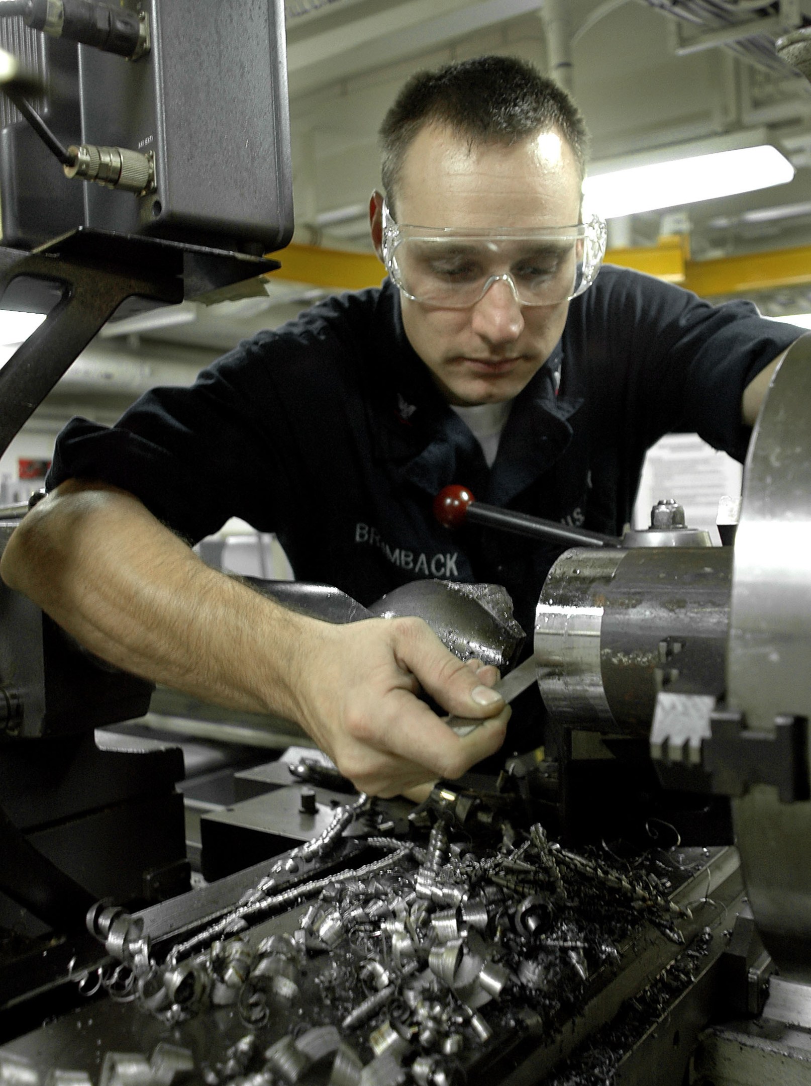 Ein Monteur mit Brille bedient eine Maschine in einer hell erleuchteten Fabrikumgebung.