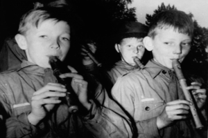 Eine Gruppe junger Jungs, die Flöten im Freien spielen, mit Bäumen im Hintergrund.