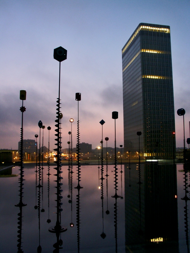 Mehrere Masten und Gebäude mit Lichtern unter einem bewölkten Himmel, mit sichtbaren Reflexionen.