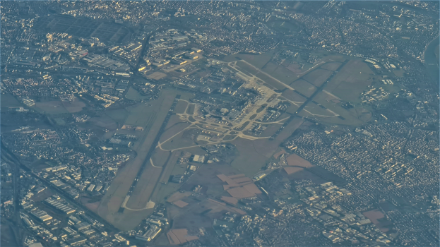 Eine Luftaufnahme eines Flughafens in einer Stadt mit Gebäuden, Straßen und Text unten.