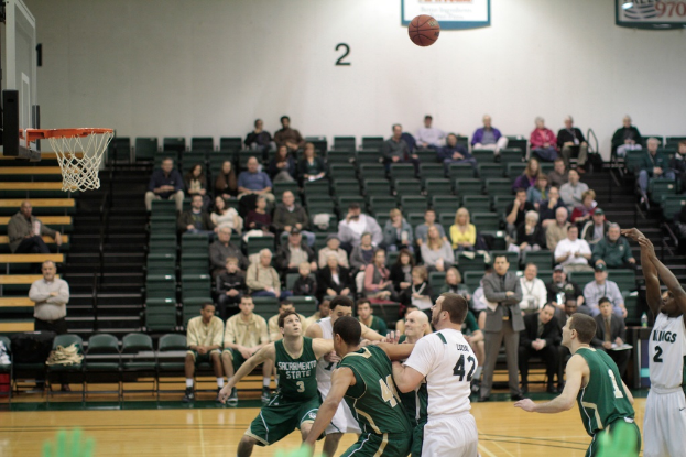 Ein Basketballfeld mit aktiv spielenden Spielern und Zuschauern im Hintergrund, die das Spiel beobachten.
