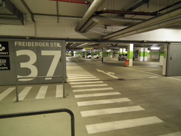 Ein Parkhaus mit einem "Freiburger St." Schild, mehrere geparkte Fahrzeuge, Säulen, ein Feuerhydrant und eine Decke mit sichtbaren Rohren.