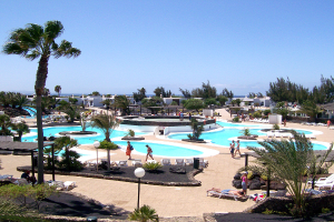 Ein Resort mit Pools umgeben von Bäumen, Menschen zwischen den Pools gehend, Gebäude im Hintergrund und ein klarer Himmel darüber.