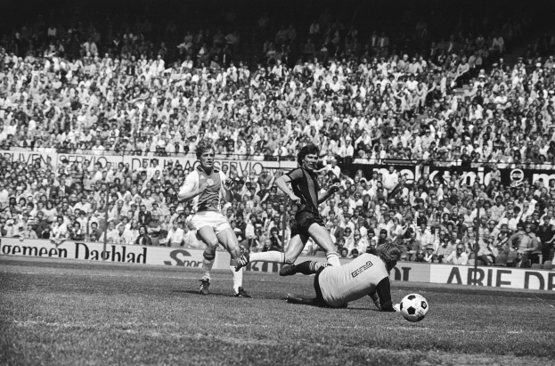 Schwarzes und weißes Foto von Fussballspielern im Einsatz auf einem Feld mit Zuschauern im Hintergrund und einer "Bundesliga 1978-79 Ajax 1-1 Hannover 96"-Tafel.