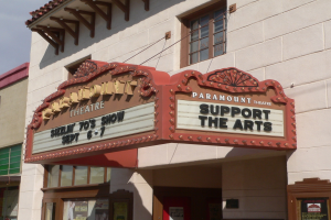 Außenansicht des Paramount Theatre in Sacramento, Kalifornien, mit Glasfenstern und -türen sowie einem "Unterstütze die Kunst"-Schild und einem sichtbaren Himmel im Hintergrund.