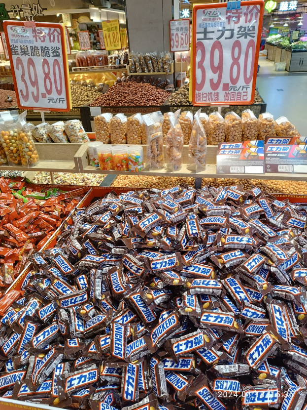 Vitrine mit verschiedenen Arten von Süßigkeiten, einschließlich Snickers-Riegeln, in einem Geschäft mit Lebensmitteln auf Regalen und Deckenbeleuchtung.