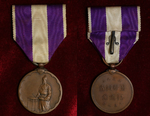 Zwei Medaillen mit lila und weißen Bändern, die beschrifteten Text tragen, auf einer maronenfarbenen Oberfläche.