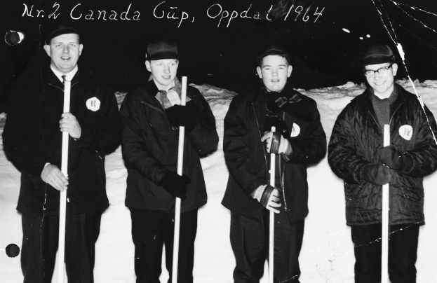 Vier Männer in Jacken und Mützen stehen im Schnee und halten Hockey-Schläger, mit dunklem Hintergrund und Text oben.