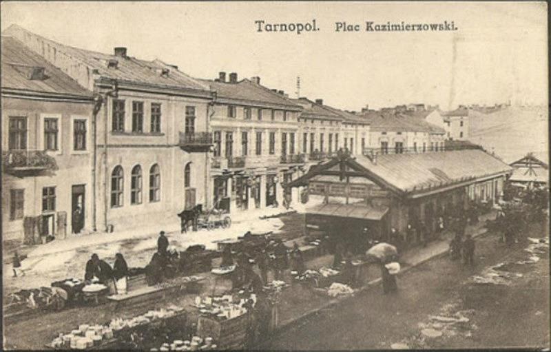 Schwarz-weiß-Foto eines belebten Marktes in Tarnopol, Polen, mit Menschen und Karren sowie Gebäuden im Hintergrund.