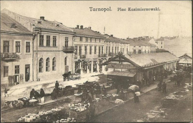 Schwarz-weiß-Foto eines belebten Marktes in Tarnopol, Polen, mit Menschen und Karren sowie Gebäuden im Hintergrund.