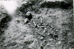 Ein Schwarz-Weiß-Foto eines Skeletts im Dreck, umgeben von Steinen und anderen Gegenständen, mit dem Text "archäologische Ausgrabung der Überreste eines Mannes" oben und unten.