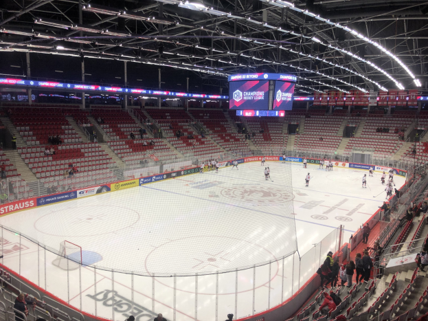 Ein Eishockeyspiel in einer großen Arena mit Zuschauern, einem Zaun um die Eisfläche, einem Display, auf dem "St. Louis Blues vs Detroit Red Wings" steht, Metallrahmen und einer Decke mit Deckenleuchten.