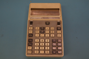 Ein Taschenrechner mit sichtbaren Tasten und Display, auf einem Tisch plaziert.