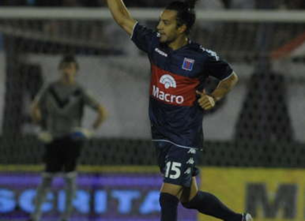 Ein Fußballspieler feiert auf dem Boden nach einem Torerfolg, mit einer jubelnden Menge und einer Person im Hintergrund, alles vor einem unscharfen, energetischen Hintergrund.