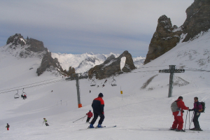 Menschen in Pullis fahren mit Skiern auf Eis mit einem Seilbahn, Bergen und einem bewölkten Himmel im Hintergrund.