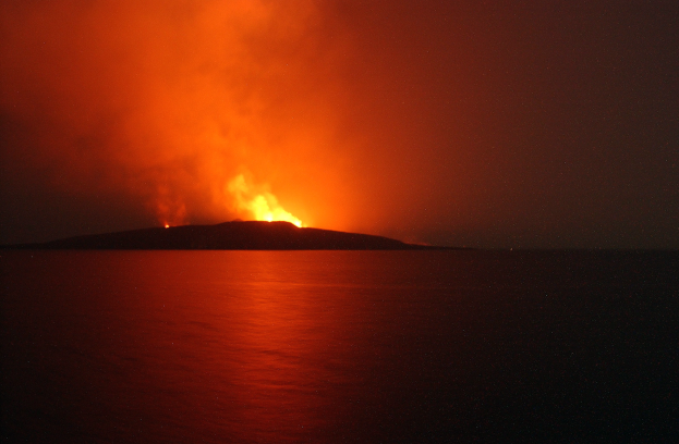 Ein Vulkan, der Lava und Rauch in den Nachthimmel speit, mit der Lava, die ins Meer fließt.